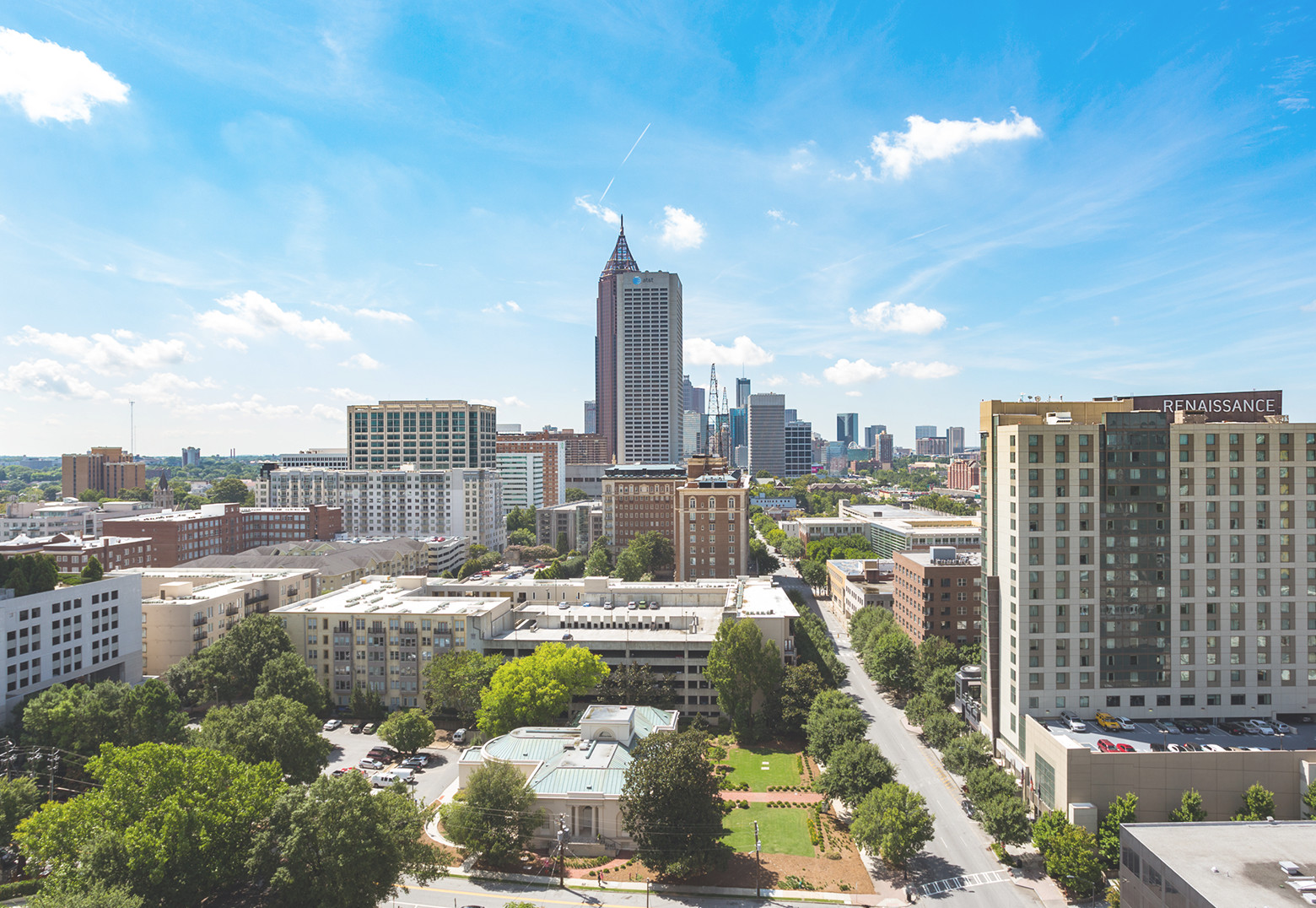 Tall city buildings surrounded by lush green trees under a clear blue sky.