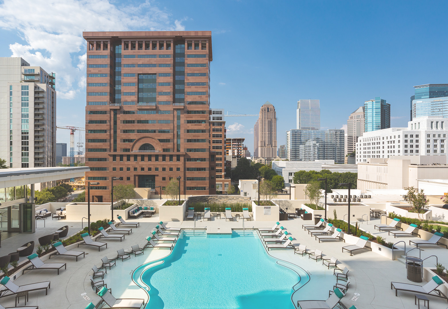 A luxurious swimming pool surrounded by comfortable swimming chairs, nestled amidst a scenic landscape of towering buildings and leafy trees.